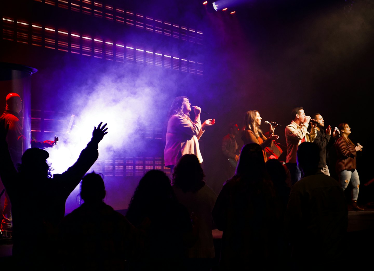 Vocalists sing into microphones on a concert stage.