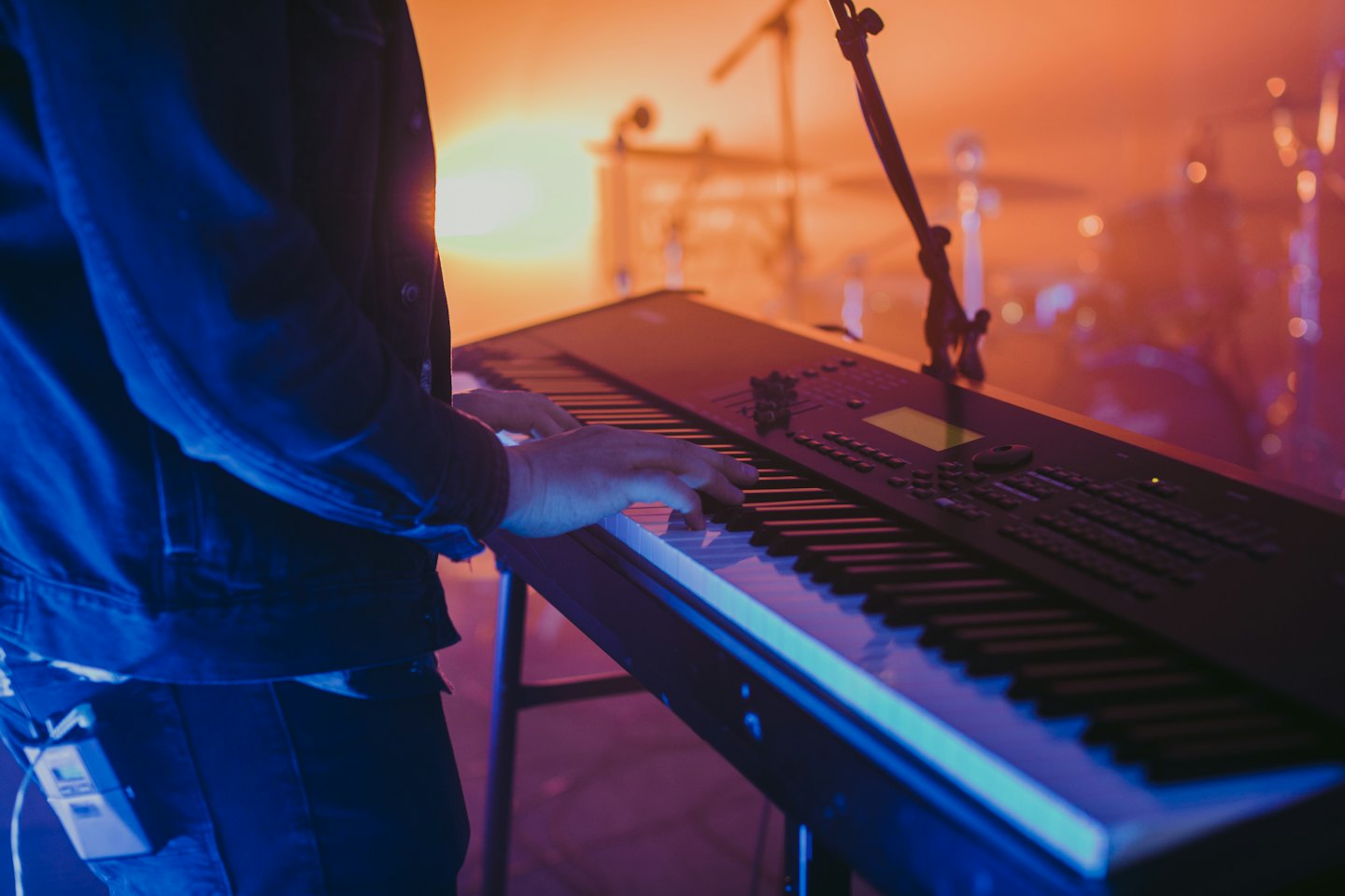 Musician playing a keyboard on a stage with colorful lights.