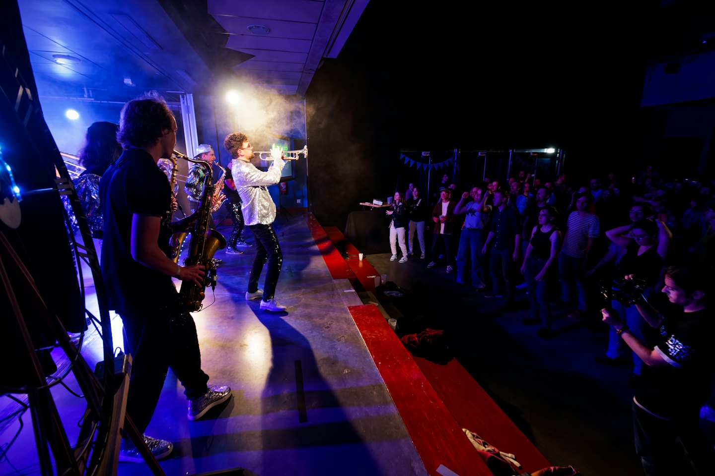 Musicians play brass instruments on a stage before an audience.