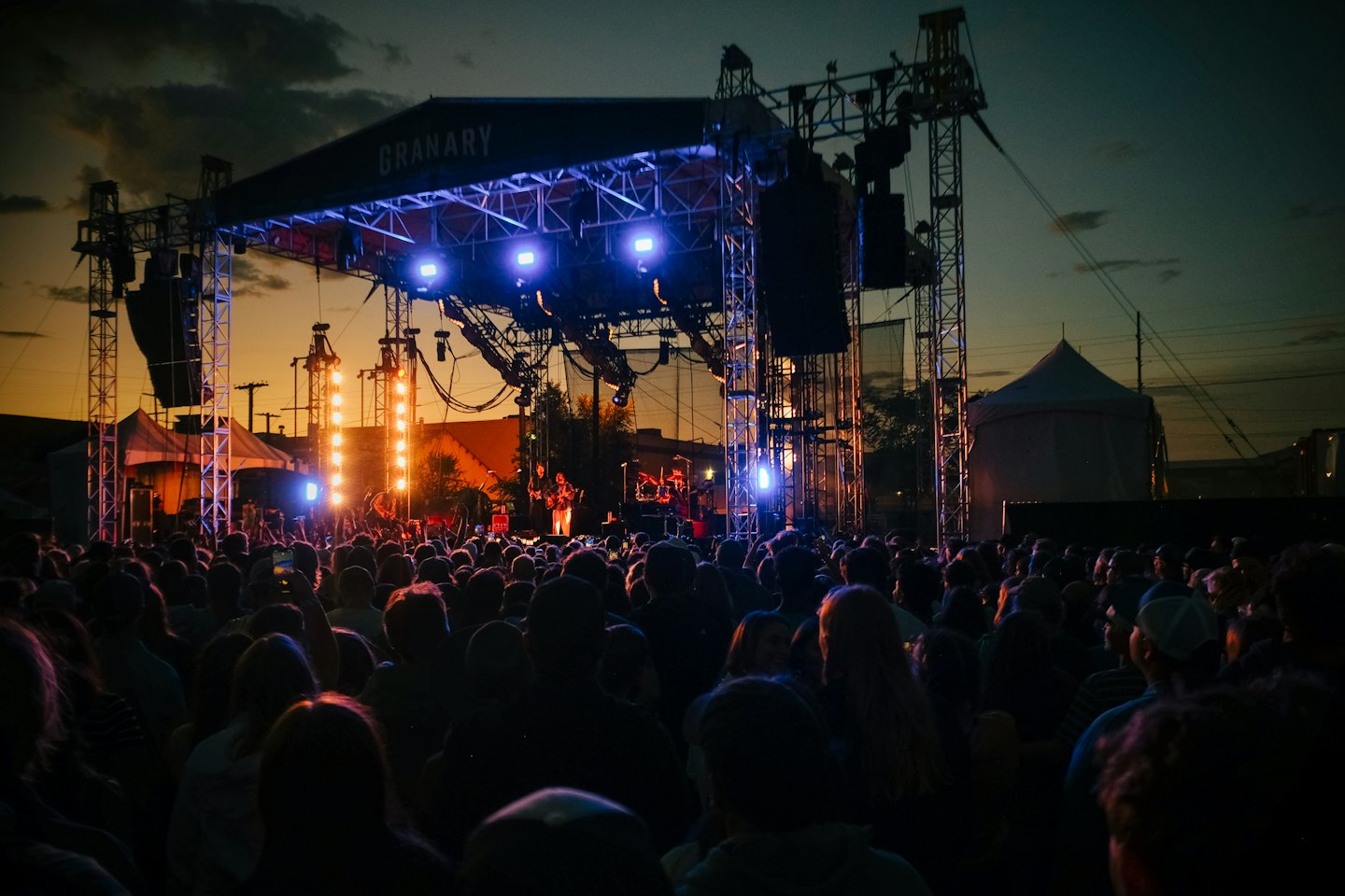 A large crowd watches a band perform on an outdoor stage.