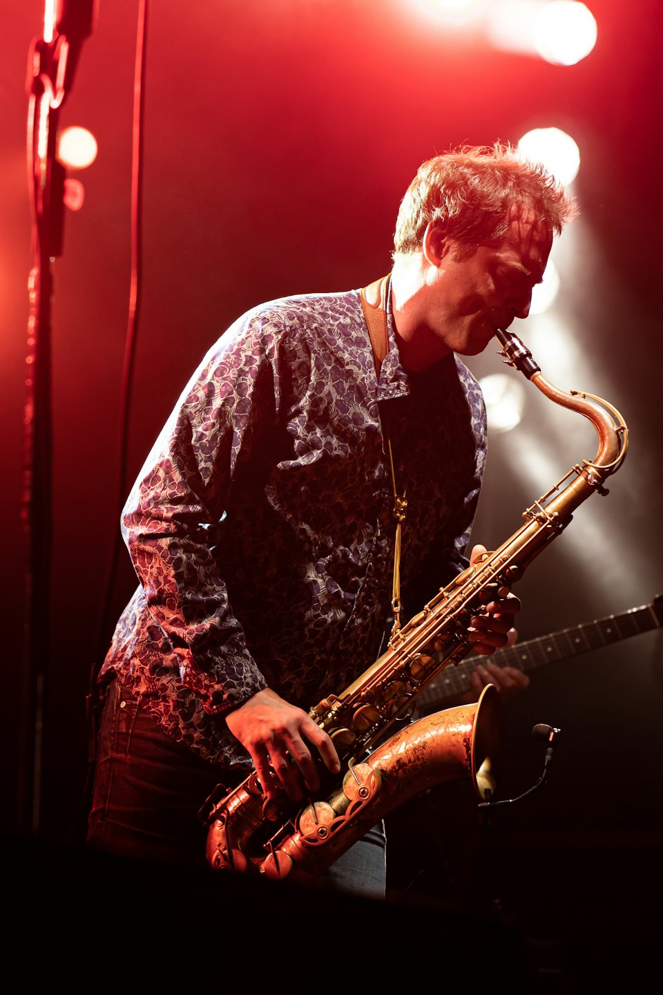 Musician plays saxophone on stage with red and orange lights.