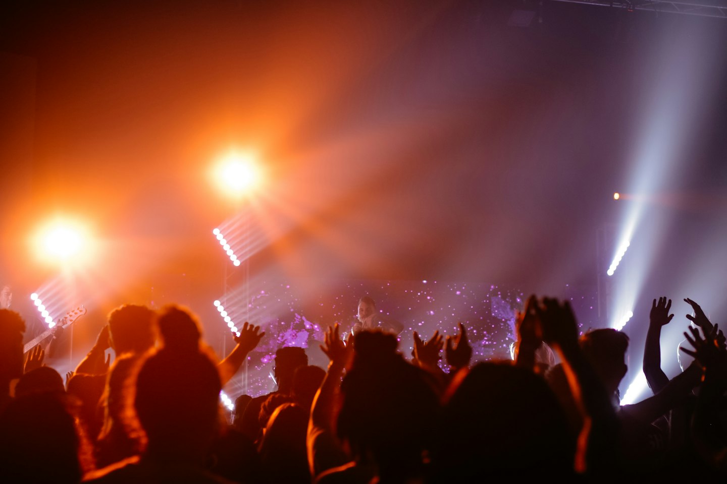 Concert audience members standing with hands raised towards a performer.