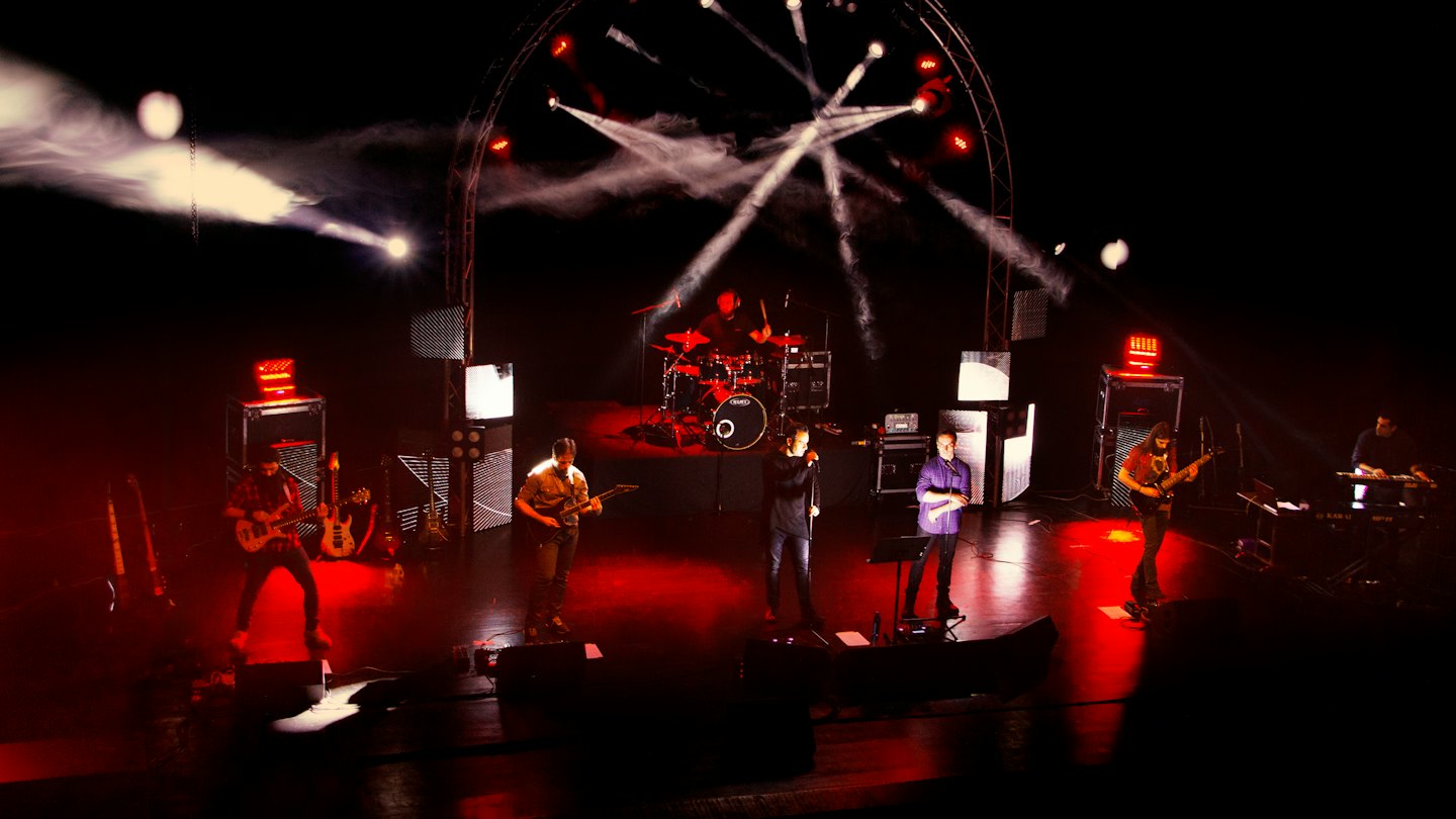 Six band members perform music together on a concert stage.