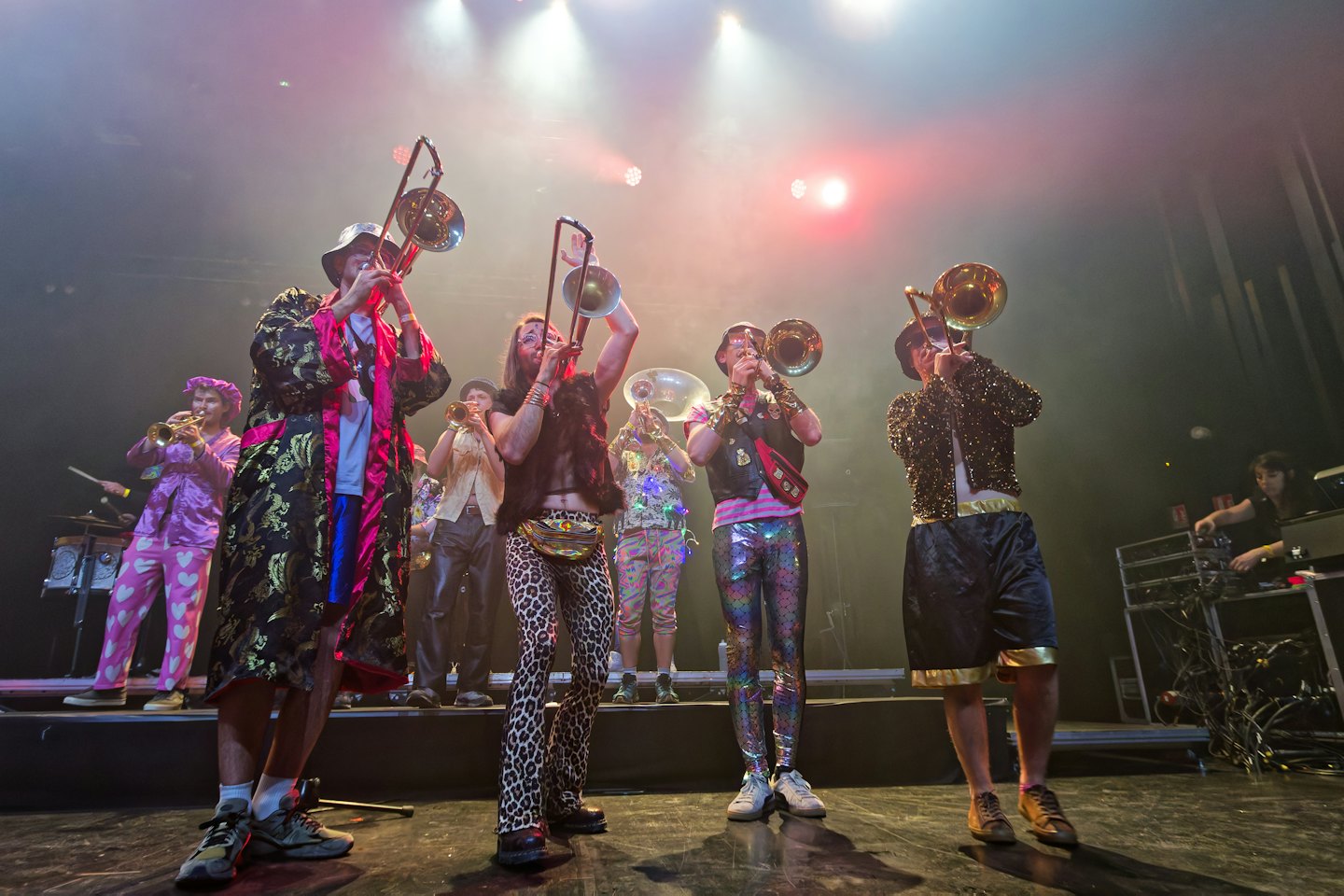 Musicians in colorful costumes play brass instruments on a stage.