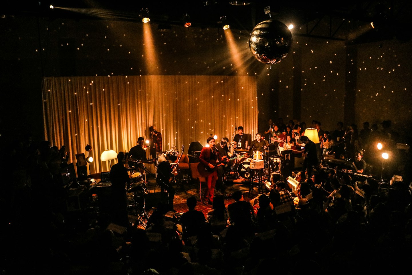 Band performing on stage with spotlights and disco ball reflections.